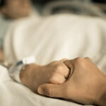 person holding hand of dying man in hospital