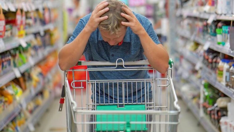 Man looking sadly at an empty shopping trolley
