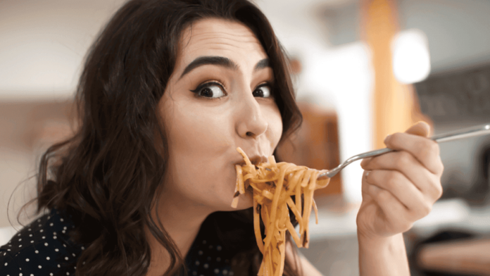 Funny young woman eating tasty pasta in cafe