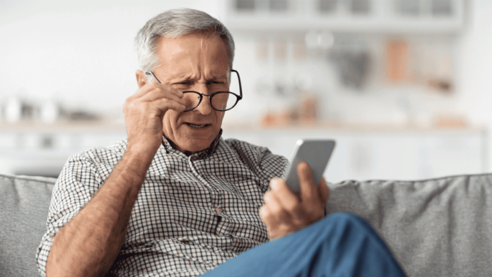 Poor Eyesight. Senior Man Squinting Eyes Reading Message On Phone Wearing Eyeglasses Having Problems With Vision Sitting On Couch At Home. Ophtalmic Issue, Bad Sight In Older Age Concept