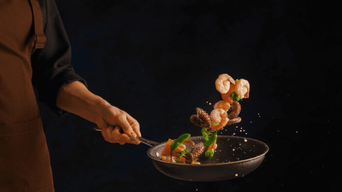 shrimp, octopus with vegetables in a frying pan on a black background by a professional chef
