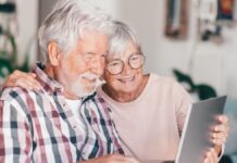 Modern happy senior white-haired couple looking together at laptop