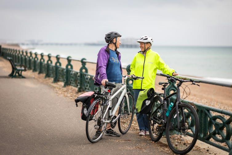 Cyclists talk, holding their bikes on a beach-front path