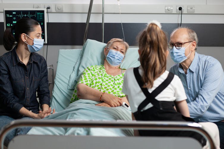 Man, woman and child visiting sick older woman in hospital, wearing masks