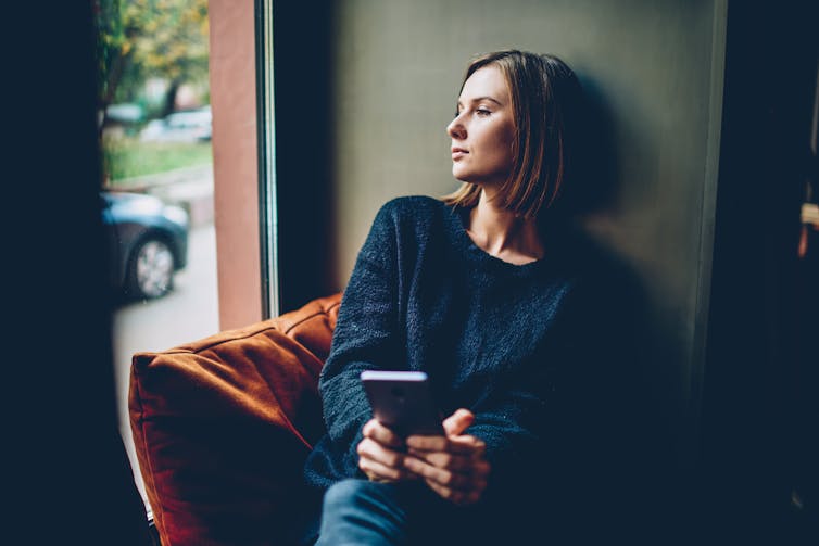 A woman looks sad while holding her phone.