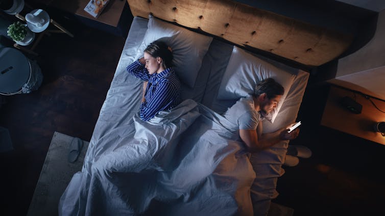 A birds-eye-view of a couple turned away from each other in bed.