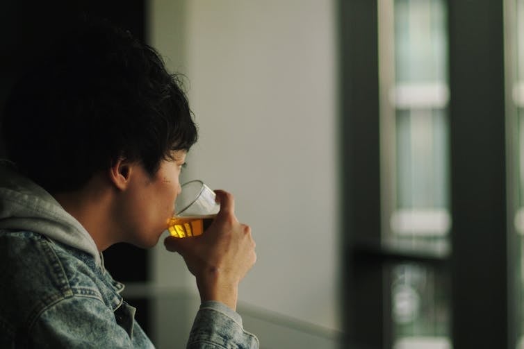 Man looks out the window drinking a beer.