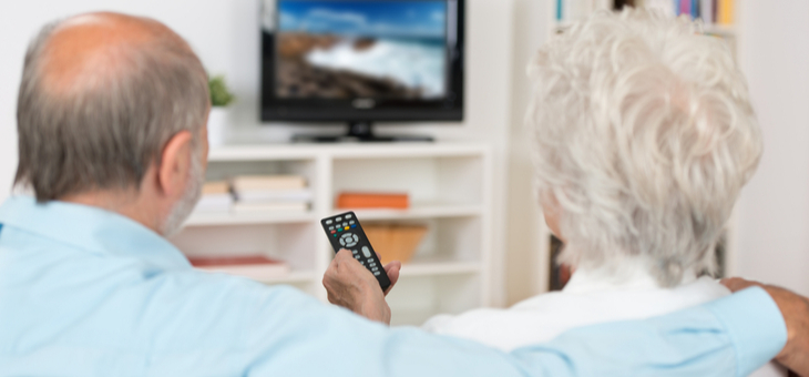 Elderly couple watching television sitting comfortably on a sofa with their backs to the camera holding the remote control