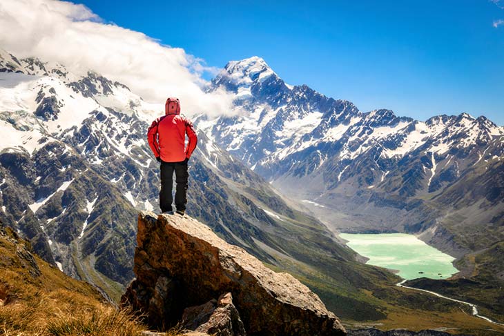 man standing on new zealand peak looking over snow capped mountains