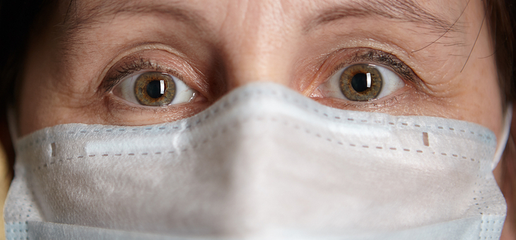Woman with medical facial surgical mask on her face, her eyes express anxiety and fear