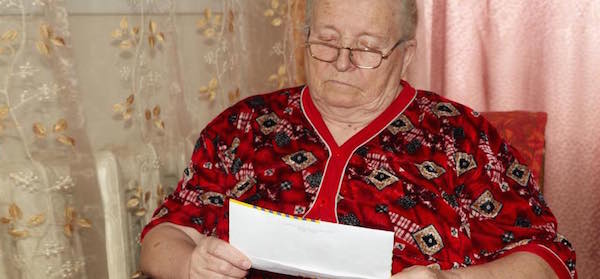 Senior woman opens a paper bill unhappily
