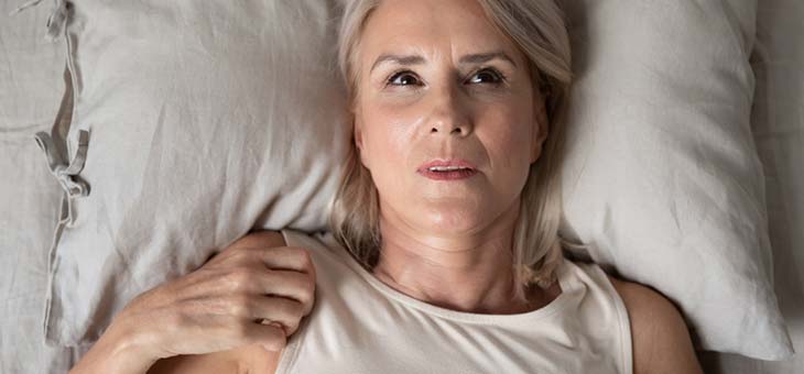 middle aged woman lying in bed thinking
