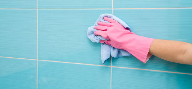 hand in pink glove cleaning a shower surface