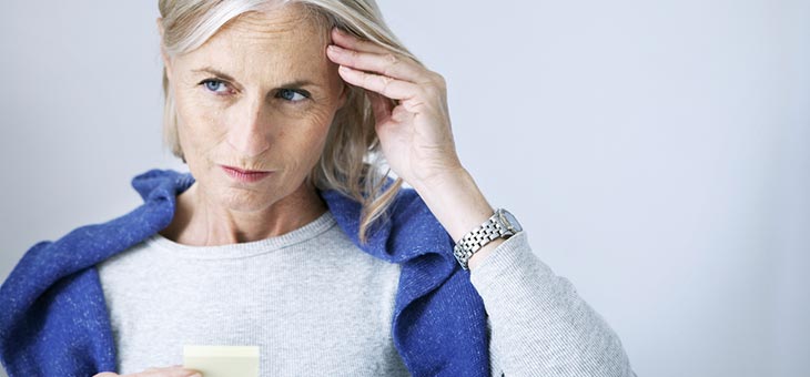older woman holding her head seemingly suffering memory loss