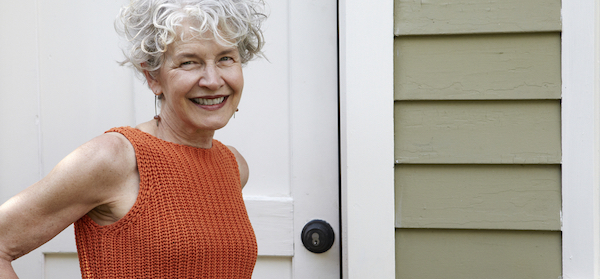 attractive mature lady standing in front of her home whilst holding on to a doorknob
