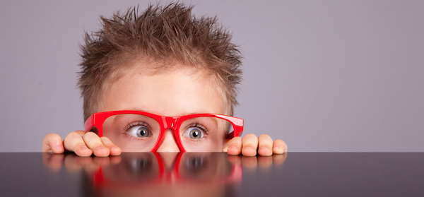Funny child wearing red glasses hiding behind a table