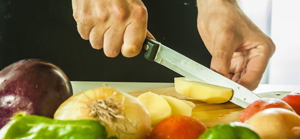 Hand cutting patatos with vegetables table