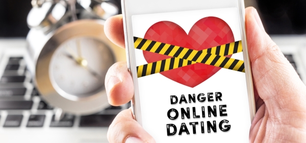 Hand holding smartphone with caution tape and the words danger online dating on screen