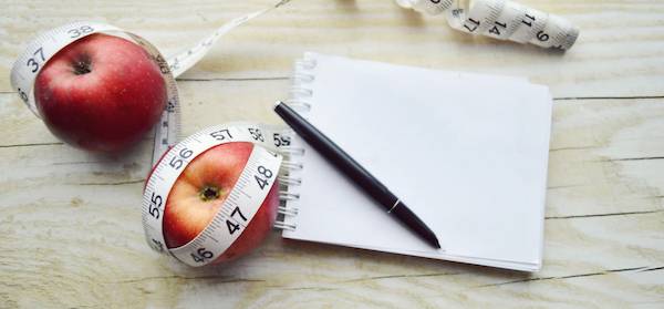 Measuring tape with healthy apples and notebook