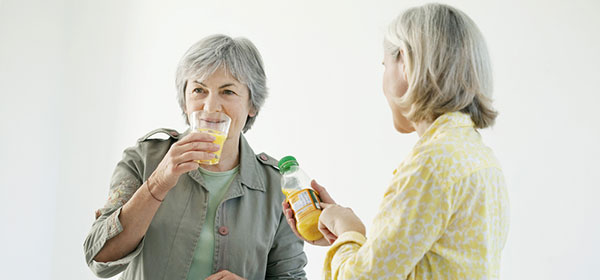two ladies talking whilst one drinks and the other checks the best before details on the side of a juice bottle